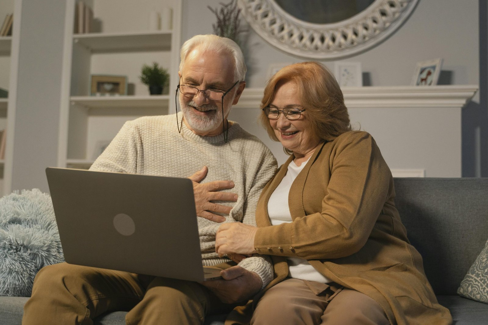 Happy senior couple sitting on a sofa having a joyful video call on a laptop in a cozy living room.